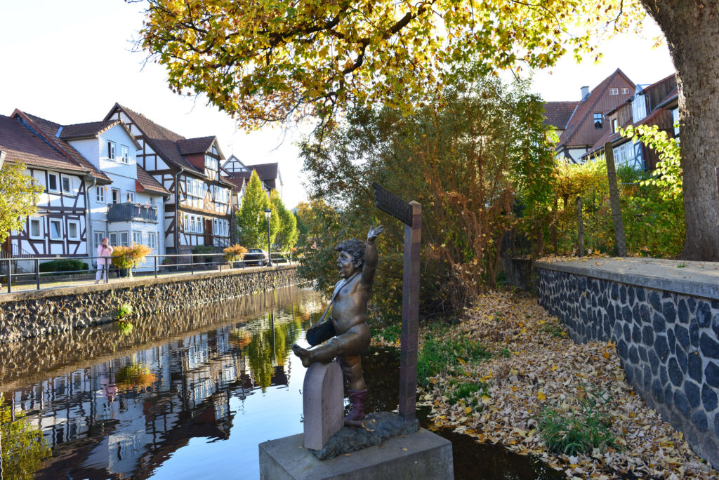Häuserreihe in Lauterbach Hessen an einem kleinen Fluss mit einer Statue und Bäumen